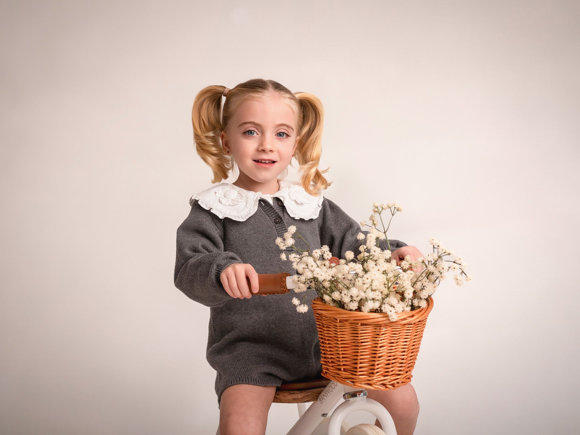 Niña con peinados de coletas y jersey gris sobre bicicleta con flores, retrato dulce y elegante.