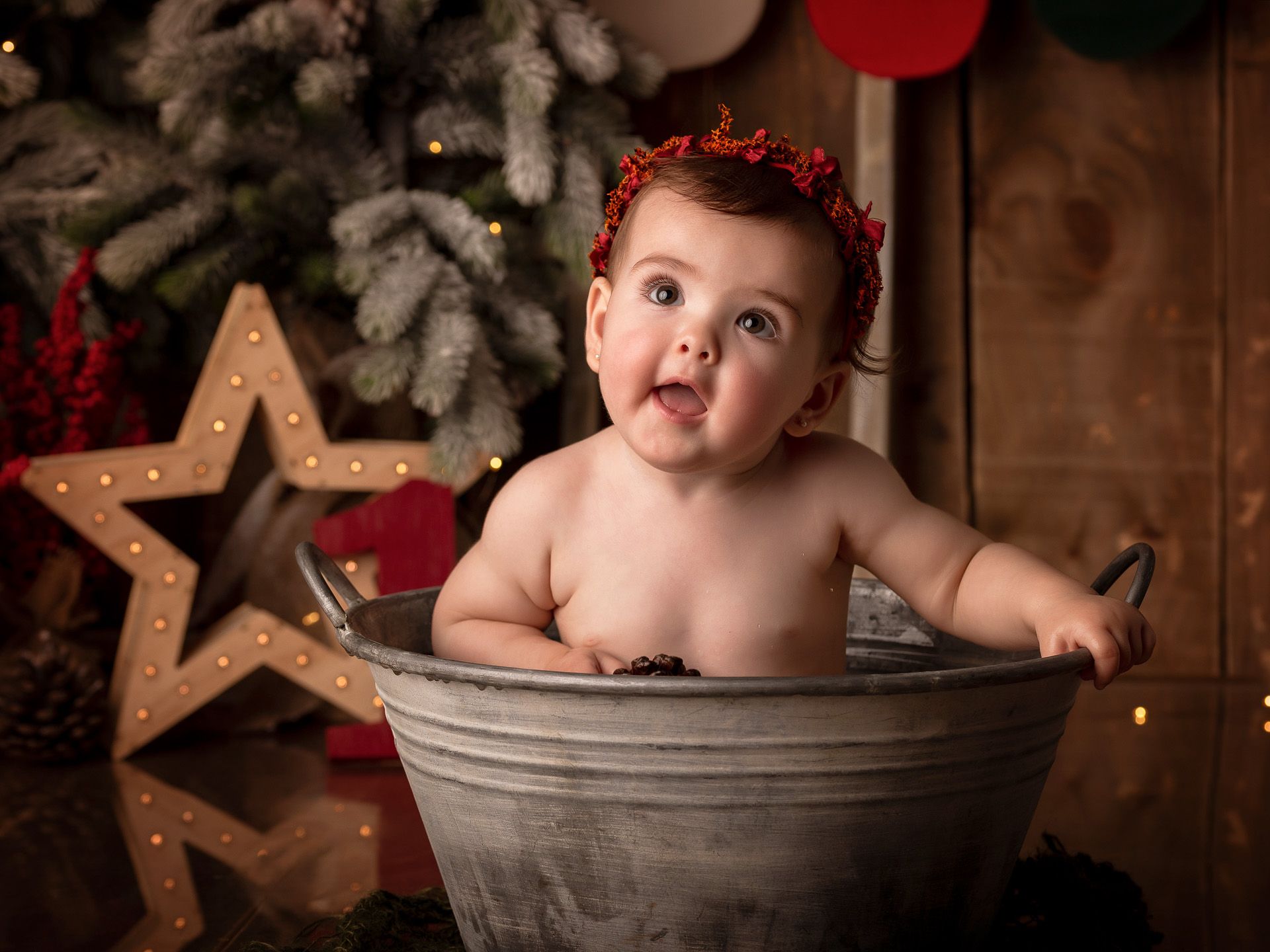 Bebé navideña en una bañera metálica mirando curiosa con fondo decorado.