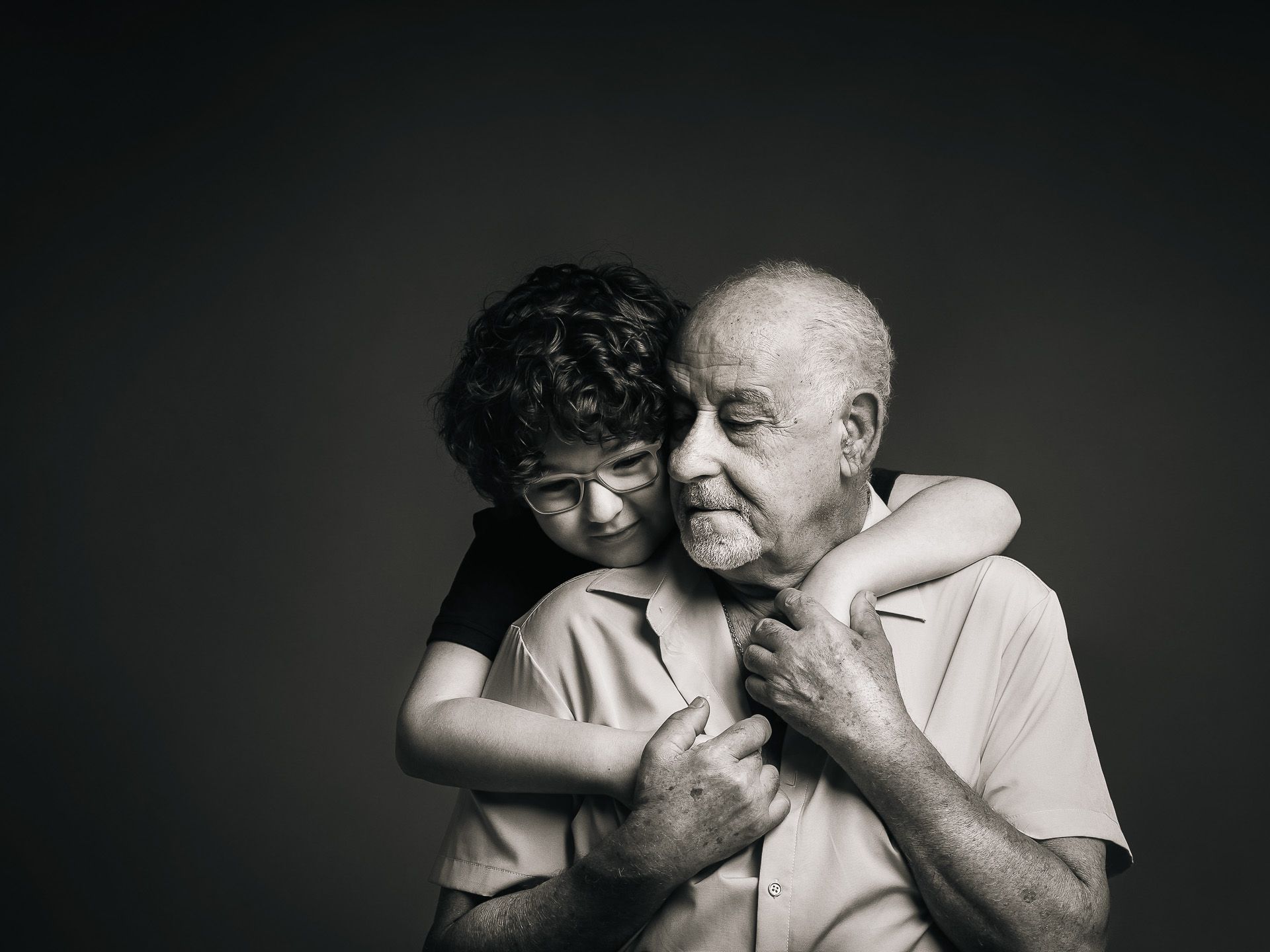 Niño abrazando por la espalda a su abuelo en un retrato íntimo y emotivo, fotografía en blanco y negro en Mérida.